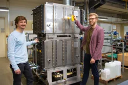 Ludwig Irrgang und Christopher Schifflechner (rechts) vor dem Prototyp der Großwärmepumpe. Bild: Susanne Höcht / TUM